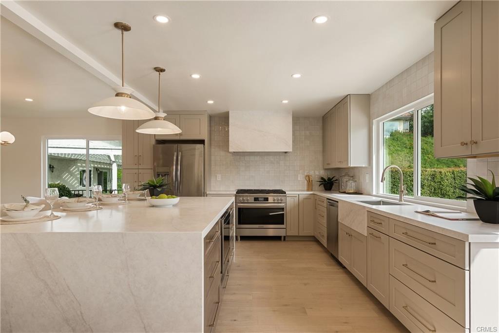 Finished kitchen: cream cabinets, brass hardware, pendants over a stone island